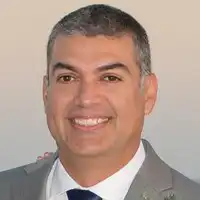 Jimmy Ramirez, a smiling man with short grey hair wearing a dark suit and white shirt