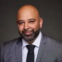 Opi Gahunia, a smiling bald man with a beard in a grey suit, white shirt and dark tie